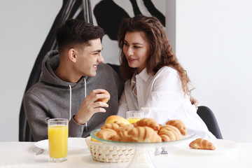 A couple of young people have breakfast with orange juice and croissants