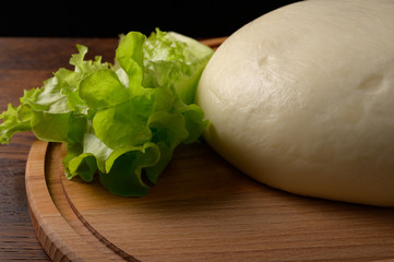 piece of national Georgian sulguni cheese with herbs on a wooden stand, close-up on a black background.