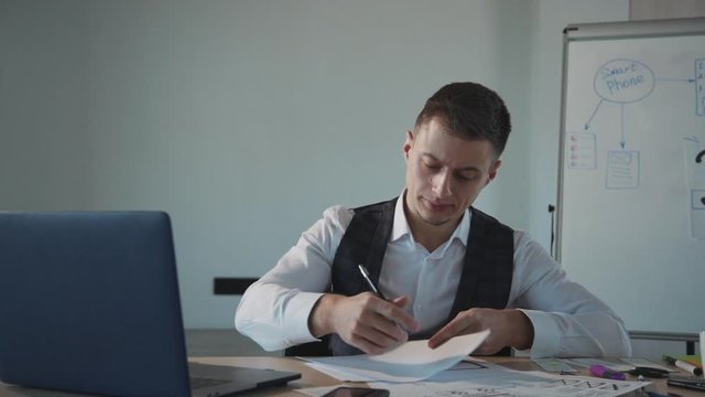 business man working on laptop computer and writing on a paper with pen. white boad with smartphone inscription on background. creating interface design. concept of ux design
