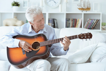 Happy senior man with guitar sitting on the sofa at home