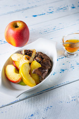 The chicken liver with the glazed apples and onions flamed in cognac on white plate. Old, wooden background. Close up. Selective focus.