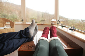 female legs in warm high socks with fur and male legs on a light closed veranda in the mountains,...