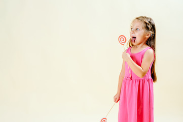 little sweet tooth. A little girl of 5 years old pulled out her tongue to lick a red big candy on a light isolated background