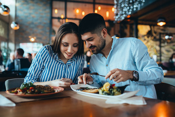 romantic couple using mobile phone while eating in restaurant