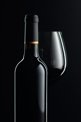 Closed bottle and glass of red wine on a black background.