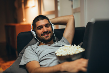 man relaxing on sofa at home using laptop and listening music