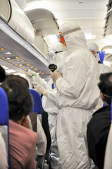 Medics in white hazmat protective suits checking and scanning passengers in a plane for epidemic...