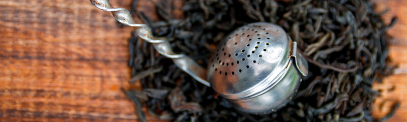 Banner of Vintage strainer with dry leaves of black tea on wooden background.