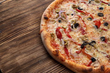 Italian pizza with red onion, black and green olives, melted cheese and ketchup on rustic textured background