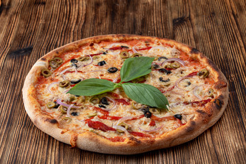 Italian pizza with red onion, black and green olives, melted cheese and ketchup on rustic textured background