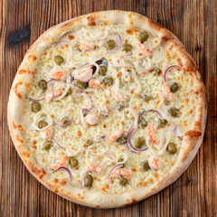 Round seafood pizza with prawns and capers on rustic textured background