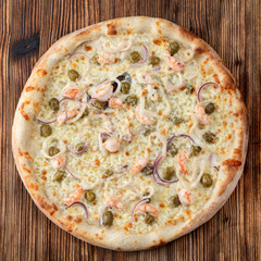 Round seafood pizza with prawns and capers on rustic textured background
