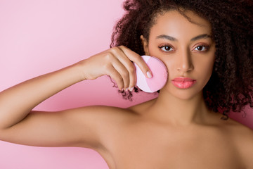Obraz na płótnie Canvas nude african american woman with closed eyes using silicone cleansing facial brush, isolated on pink