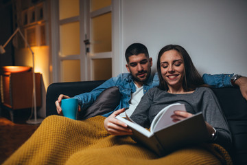 happy couple reading book relaxed in sofa at home
