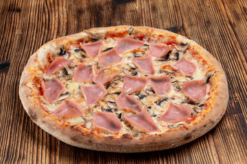 Baked pizza with golden crust, ham, champignons and melted cheese