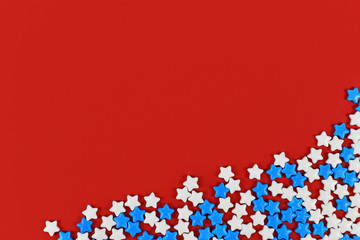 White abd blue star shaped sugar sprinkles on bright red background with blank copy space
