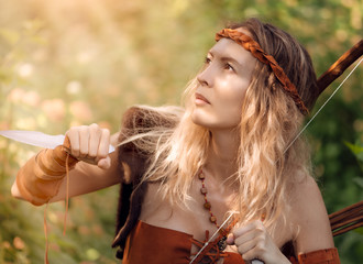 Beautiful girl archer with long blond hair with bow and arrowson a back holding two steel knifes...