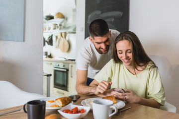 Obraz na płótnie Canvas happy couple using smartphone while having breakfast at home