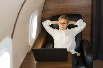 beautiful stylish woman in age, in the cabin of a private jet lies in a chair