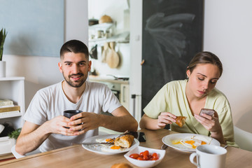 Fototapeta na wymiar romantic couple eating breakfast at home, man using cell phone
