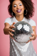 Naklejka premium selective focus of happy african american girl in paillettes dress holding disco ball, isolated on pink