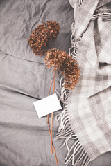 Dried flowers romantic bouquet and white empty card stack on bed. Original and beautiful flowers posy on the gray bedings with plaid. Cozy bedroom. Close up photo.