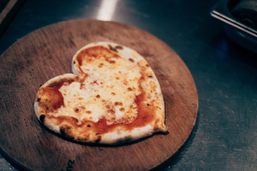 heart shaped pizza from the oven on a round wooden board