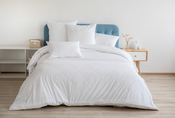 Interior with white bed linen on the sofa. Bedroom with bed, white bedding, and bedside table. White pillows, duvet and duvet case on bed with blue headboard. Front view. - obrazy, fototapety, plakaty