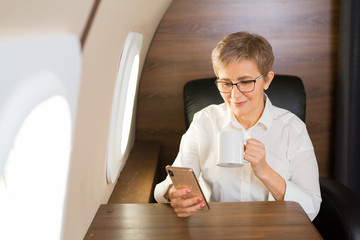 beautiful stylish woman aged, in the cabin of a private plane with a phone in her hand