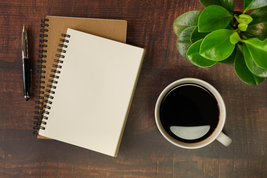 Top view of open school notebook with blank pages, Pen, Plant and Coffee cup on wooden table background. Business, office or education concept with copy space.