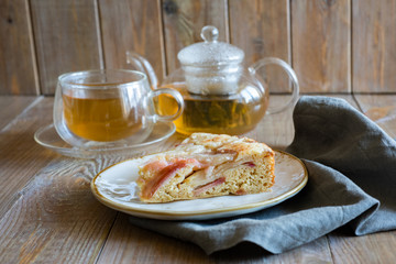 A slice of Apple pie on a vintage plate in the background, a Cup of green tea and a glass teapot with tea in the background