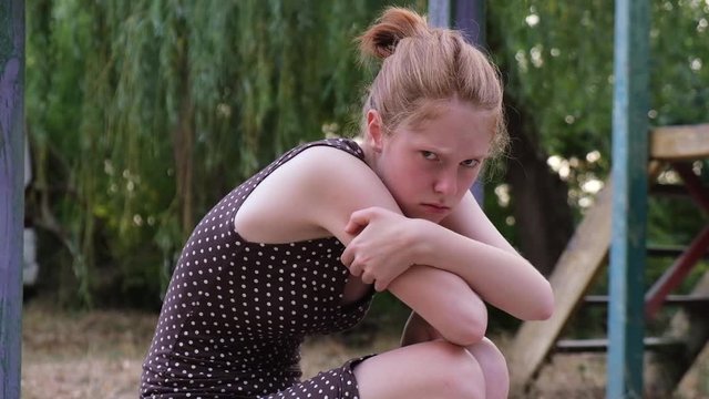 Offended girl sitting on a bench at the playground. Young lady indignant and yelling at parents