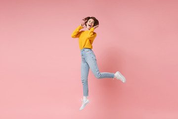 Fototapeta na wymiar Cheerful laughing young brunette woman girl in yellow sweater posing isolated on pastel pink wall background in studio. People lifestyle concept. Mock up copy space. Having fun fooling around jumping.