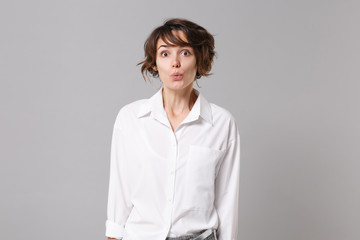 Shocked amazed young brunette business woman in white shirt posing isolated on grey wall background...