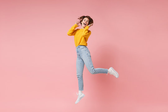 Cheerful laughing young brunette woman girl in yellow sweater posing isolated on pastel pink wall background in studio. People lifestyle concept. Mock up copy space. Having fun fooling around jumping.