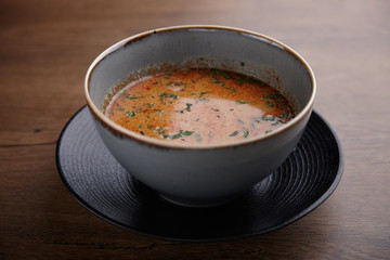 Tomato soup with herbs in a ceramic plate on a dark wooden table.
