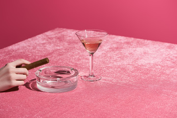 cropped view of woman holding cigar near ashtray and glass of rose wine on velour cloth isolated on...