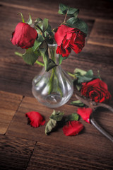 Withered rose on dark gray background and wooden table with fall petals and leaves, design concept of sad Valentine's day romance, broken up, copy,space.