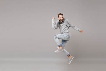 Young bearded man in gray sweater, scarf posing isolated on grey wall background, studio portrait. Healthy fashion lifestyle, cold season concept. Mock up copy space. Jumping, doing winner gesture.