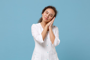 African american doctor woman isolated on blue background. Female doctor in white medical gown sleep with folded hands under cheek. Healthcare personnel health medicine concept. Mock up copy space.