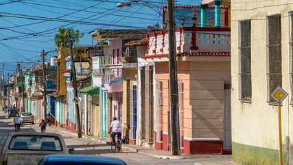 old trinidad street with many colorful houses, cars and people, cuba	