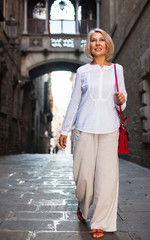 Fototapeta na wymiar Cheerful mature female is walking in white blouse on the street outdoor