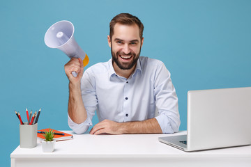 Smiling young bearded man in light shirt sit and work at white desk with pc laptop isolated on...