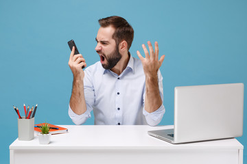 Angry nervous young bearded man in light shirt work at white desk with pc laptop isolated on pastel...