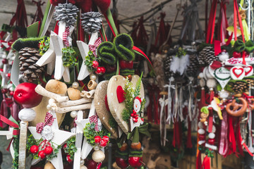 Naklejka premium Traditional Christmas decorations for sale at a Christmas market stand on a sunny winter day in December. Red and green hanging toys and decorations. Close up shot