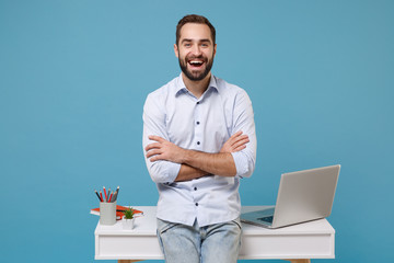 Laughing young bearded man in light shirt work near white desk with pc laptop isolated on pastel...