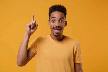 Excited young african american guy in casual t-shirt posing isolated on yellow orange background in studio. People lifestyle concept. Mock up copy space. Holding index finger up with great new idea.
