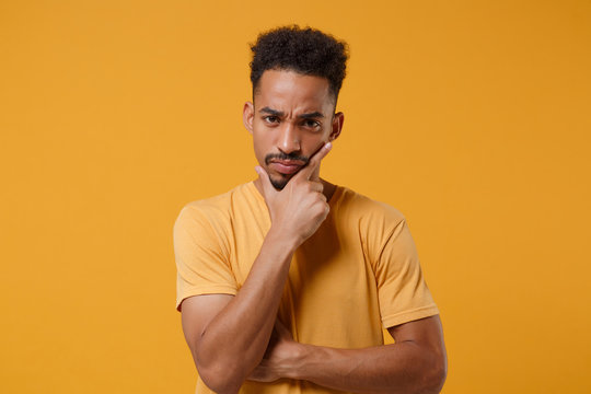Preoccupied young african american guy in casual t-shirt posing isolated on yellow orange background studio portrait. People emotions lifestyle concept. Mock up copy space. Put hand prop up on chin.