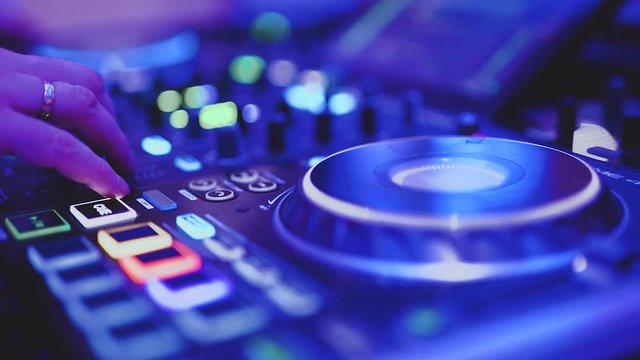 DJ hand mixing music at a party on colorful mixing board, close up