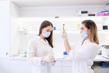 Two young beautiful women lab workers examine tests of a new drug for oncology and record the results. Concept of new innovative effective agents for the treatment of complex diseases